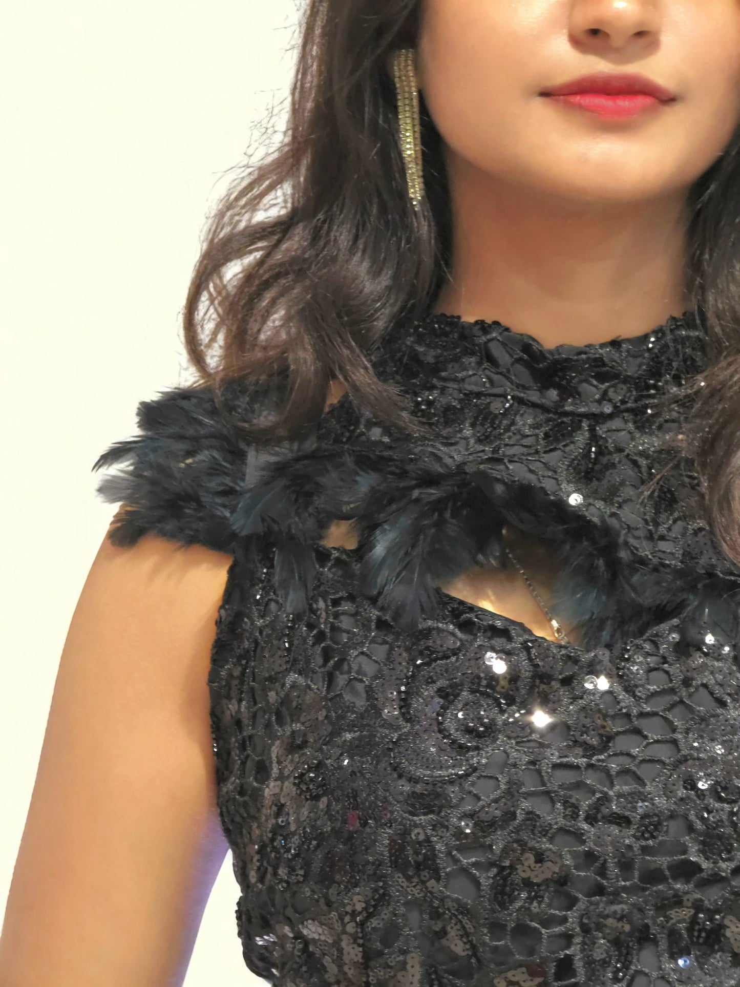Close-up of a person wearing a black sequin dress with feather details.