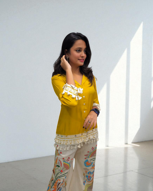 Woman wearing a yellow top with white details and patterned pants in a bright room.
