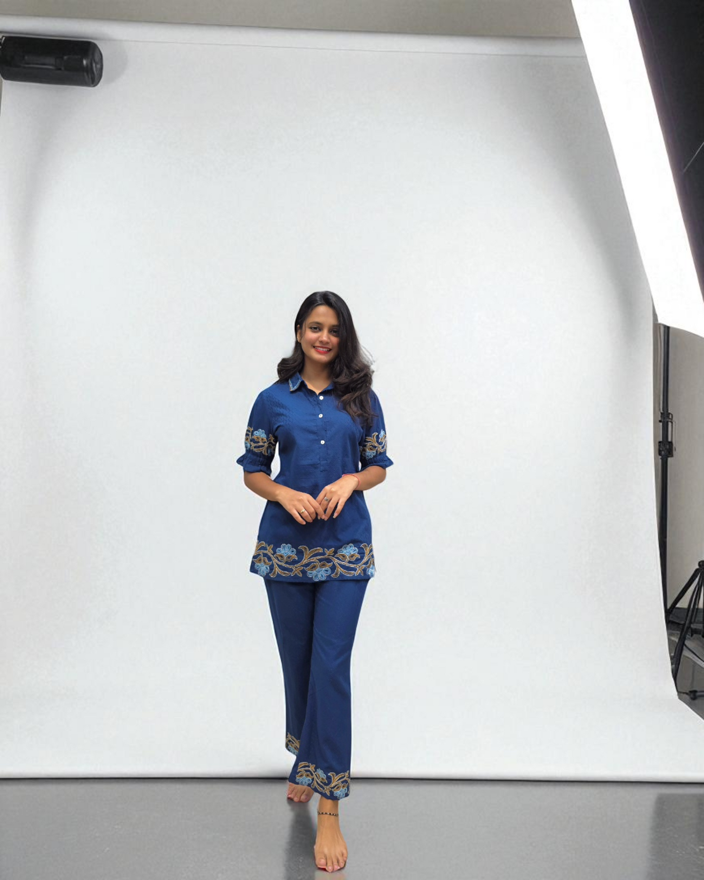 "Woman wearing a stylish blue embroidered co-ord set with palazzo pants, featuring floral detailing on the hem and sleeves, standing barefoot against a clean white background."