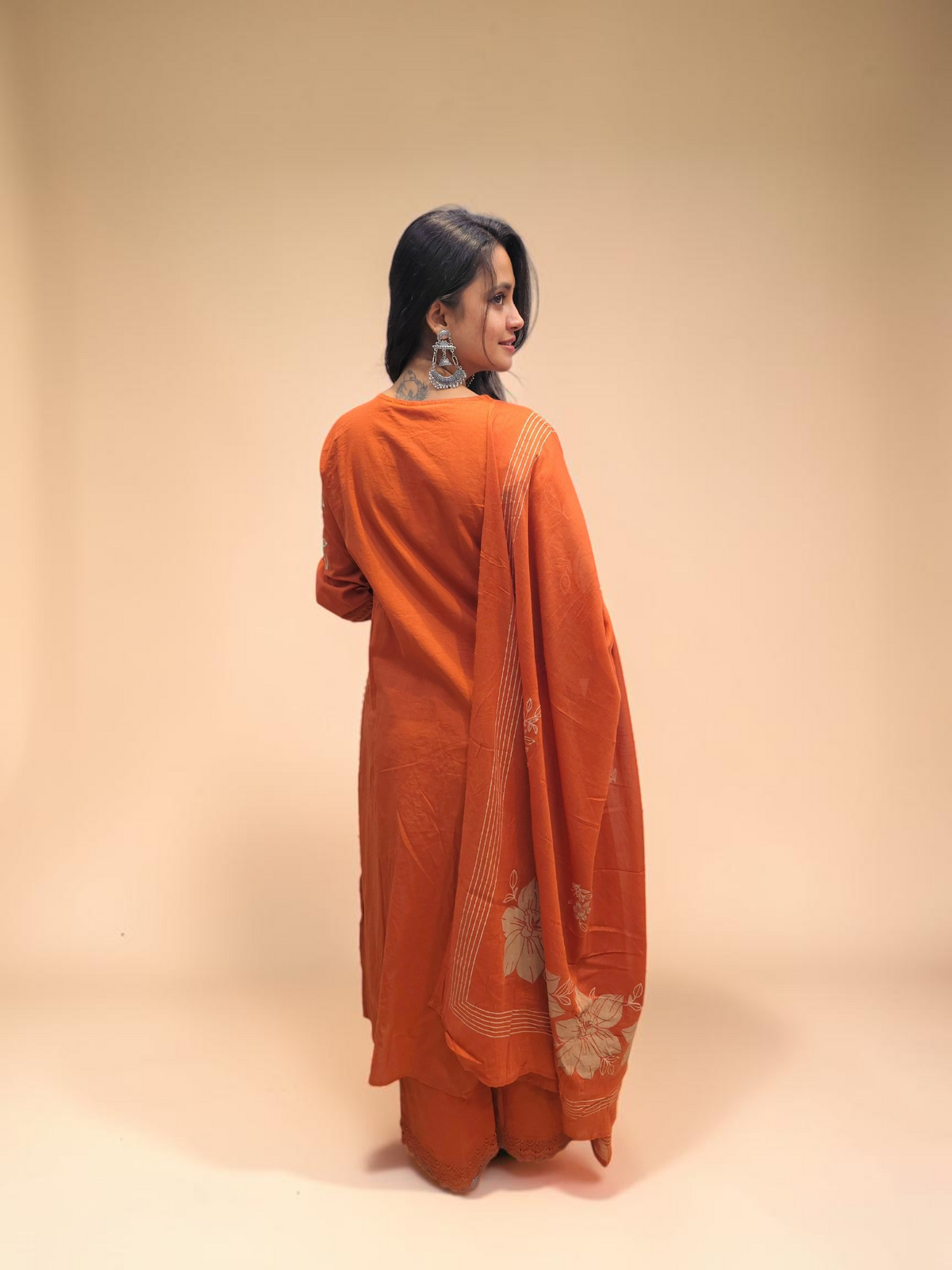 Back view of A woman wearing a burnt orange kurta and matching trousers with a matching dupatta draped over her shoulder.