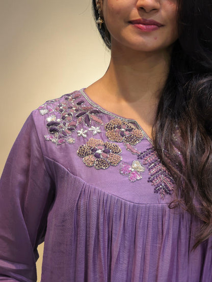A close-up of a woman wearing a lavender purple tunic top with intricate floral embroidery and beadwork on the neckline.