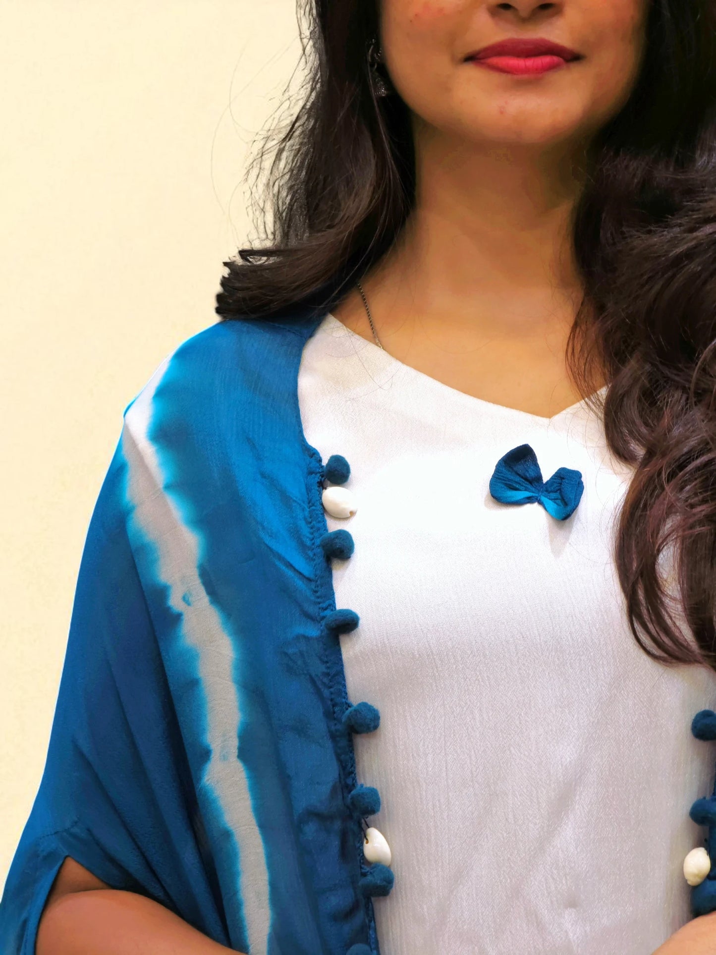 Woman wearing a blue and white outfit with a blue bow detail on a beige background
