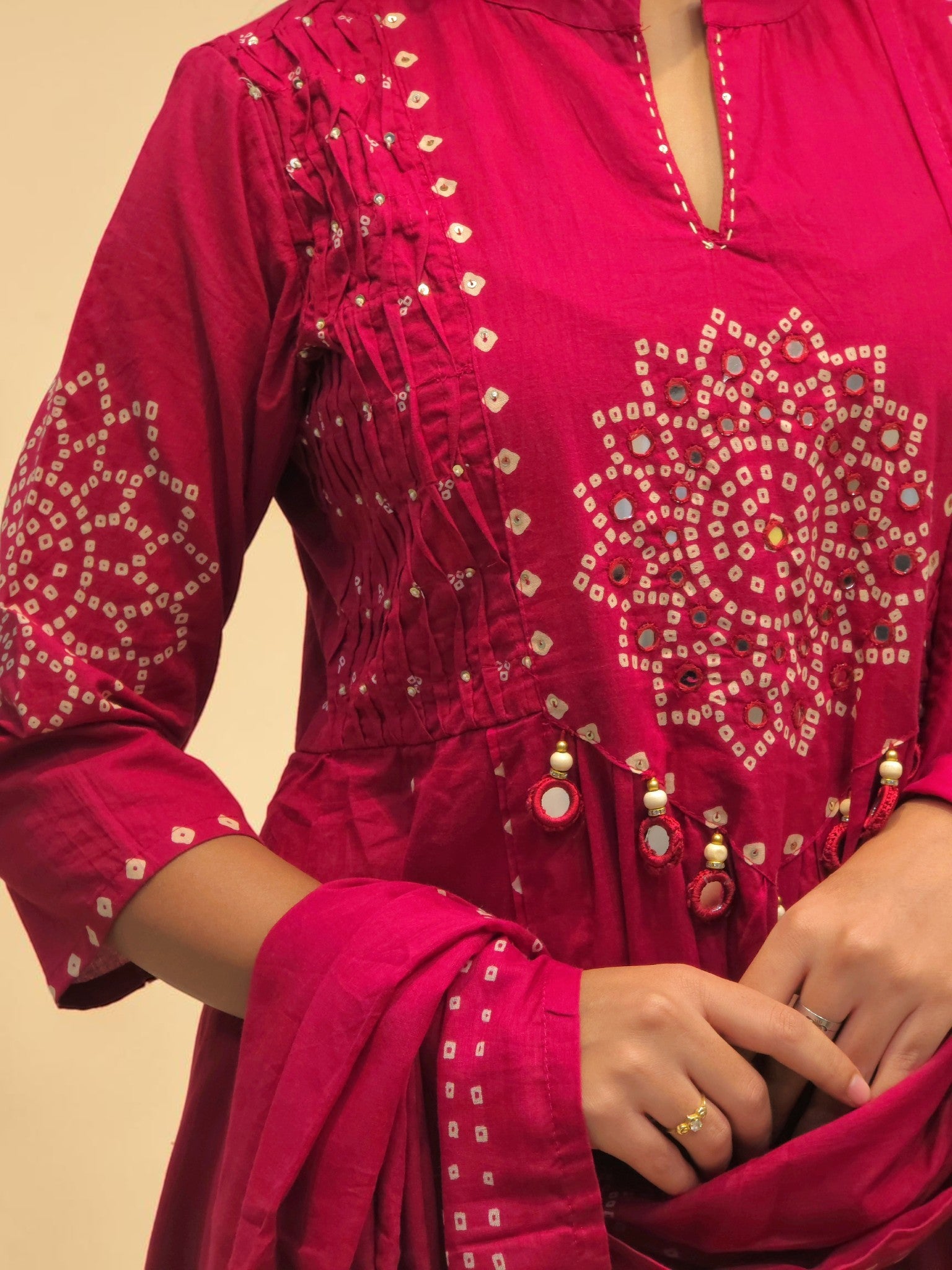A close-up of a person wearing a bright pink traditional embroidered kurta with white geometric bandhani-style prints, decorative mirror work, and a matching dupatta.