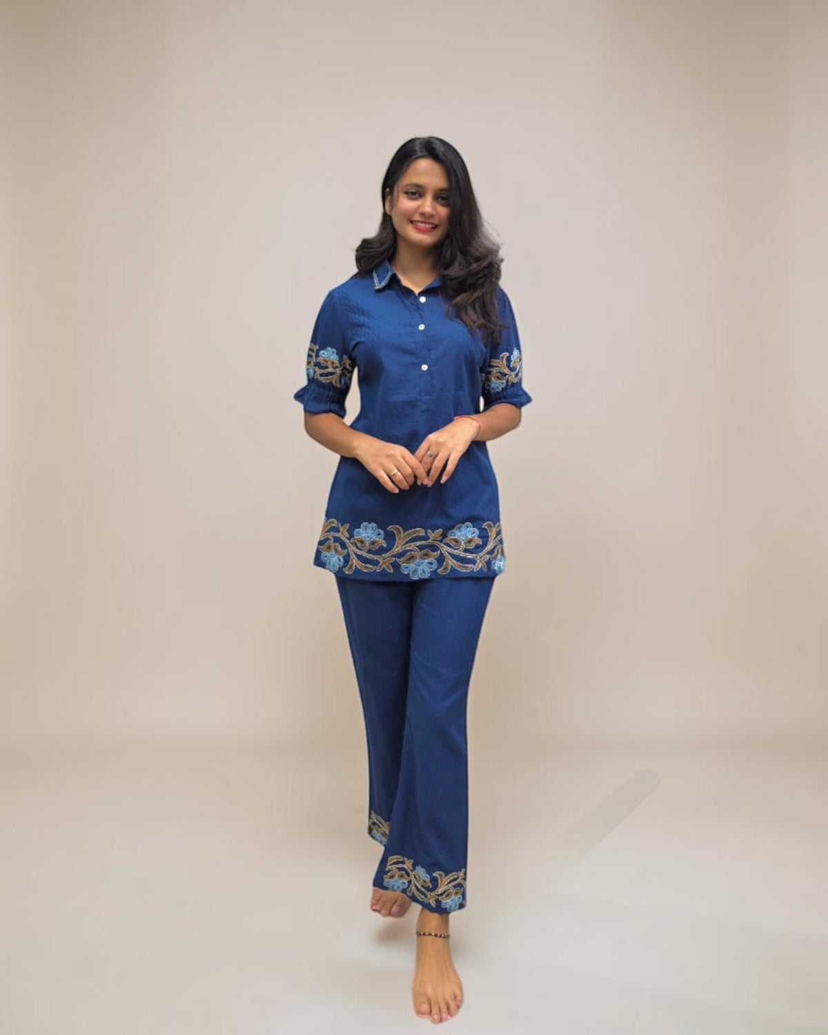 "Woman wearing a stylish blue embroidered co-ord set with palazzo pants, featuring floral detailing on the hem and sleeves, standing barefoot against a clean white background."